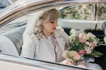 bride in Cadillac with bouquet of flowers wearing a crown and a white denim jacket over her bridal dress